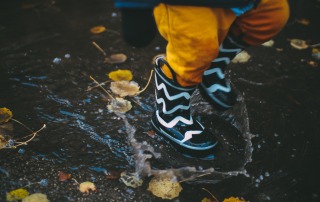 Kid jumping in a puddle wearing rubber boots