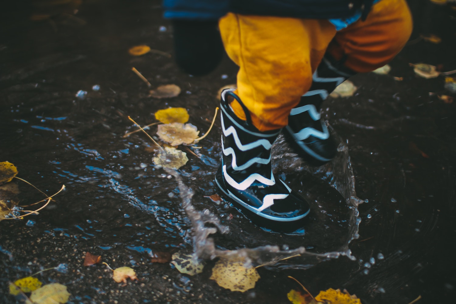Kid jumping in a puddle wearing rubber boots